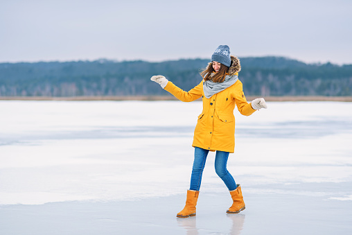 A beautiful smiling girl in a yellow winter jacket, warm hat and boots having fun in the middle of a frozen lake.