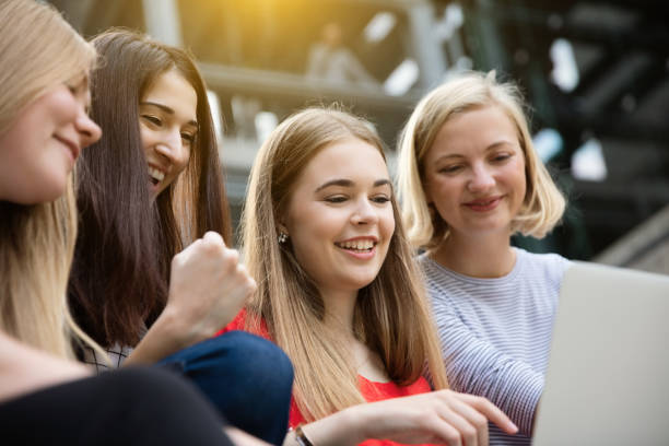 istock Young female friends using laptop while sitting on steps outdoors 887522974