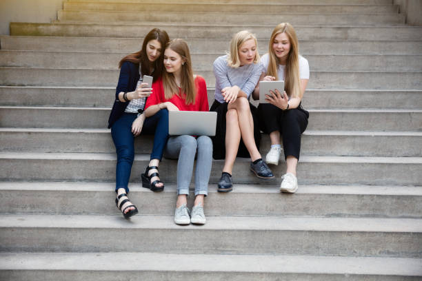 istock Young female friends using laptop while sitting on steps outdoors 887523066