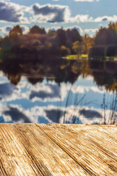 istock Empty rustic wood table top on  blurred colorful autumn landscape background with fall forest and blue sky with cloudscape reflection on the lake. Can montage or display your products 887549862