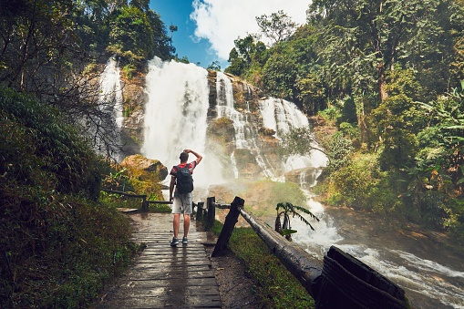 Young man (traveler) standing near Wachirathan waterfall in tropical rainforest. Chiang Mai Province, Thailand