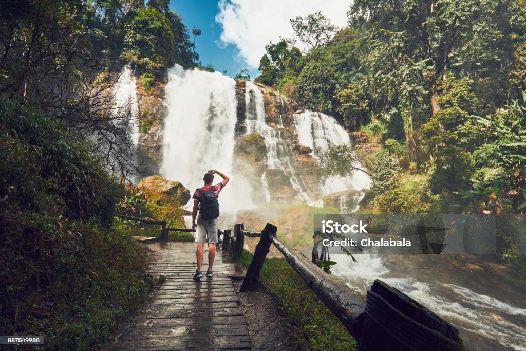 Traveler near waterfall Young man (traveler) standing near Wachirathan waterfall in tropical rainforest. Chiang Mai Province, Thailand Waterfall Stock Photo