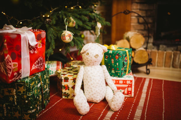 istock Teddy bear sitting under decorated with lights Christmas tree with gift boxes 887558570