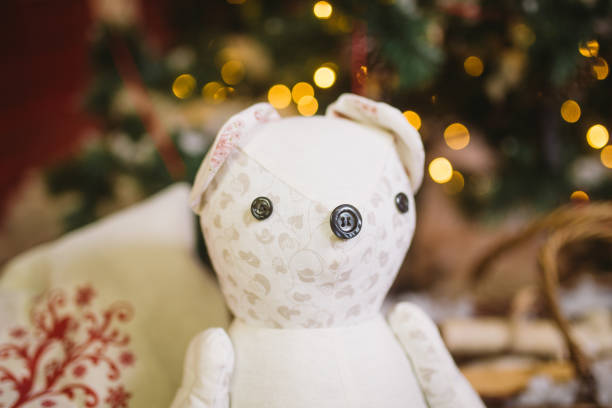 Teddy bear sitting under decorated with lights Christmas tree with gift boxes