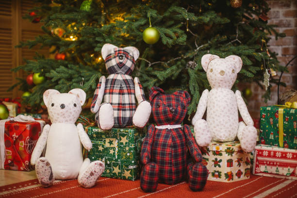 istock Teddy bear sitting under decorated with lights Christmas tree with gift boxes 887559188