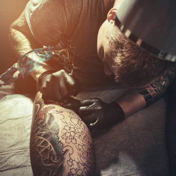 istock Tattoo master making tattoo on customer's leg 887569404