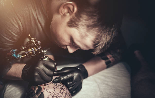istock Tattoo master making tattoo on customer's leg 887571910