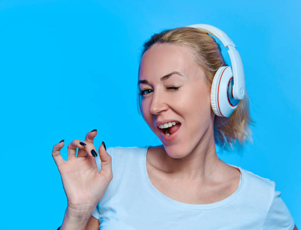 blondynka ze słuchawkami słuchającymi muzyki i gumą do żucia na niebieskim tle - chewing gum audio zdjęcia i obrazy z banku zdjęć