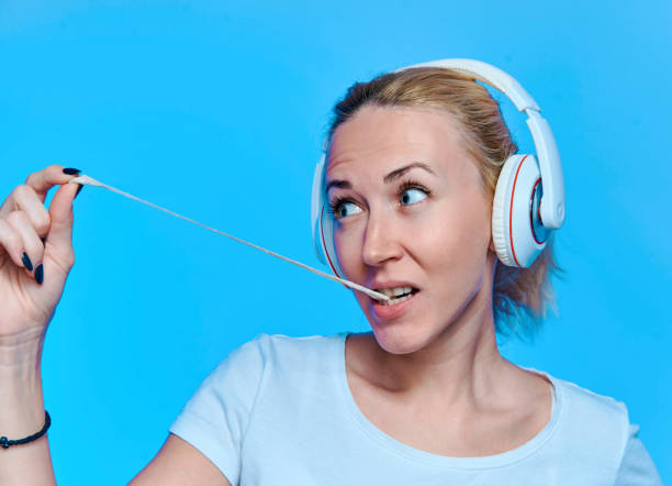 blondynka ze słuchawkami słuchającymi muzyki i gumą do żucia na niebieskim tle - chewing gum audio zdjęcia i obrazy z banku zdjęć