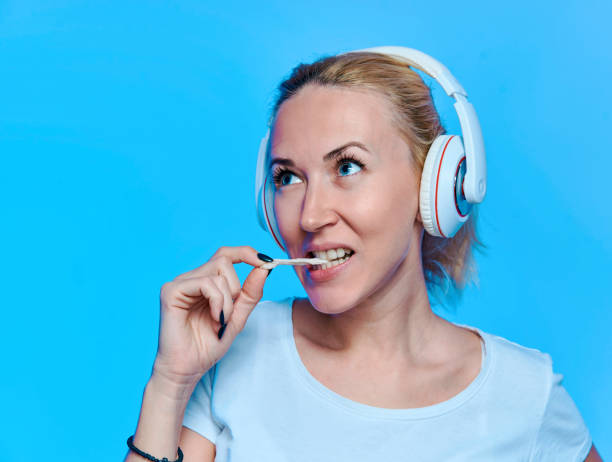 blondynka ze słuchawkami słuchającymi muzyki i gumą do żucia na niebieskim tle - chewing gum audio zdjęcia i obrazy z banku zdjęć