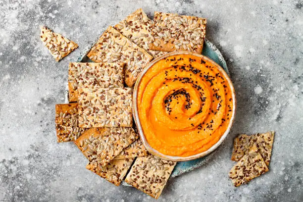 Pumpkin hummus seasoned with olive oil and black sesame seeds with whole grain crackers. Healthy vegetarian appetizer or snack