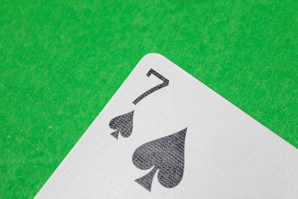 Close up shot of a playing card on a green surface, seven of spades