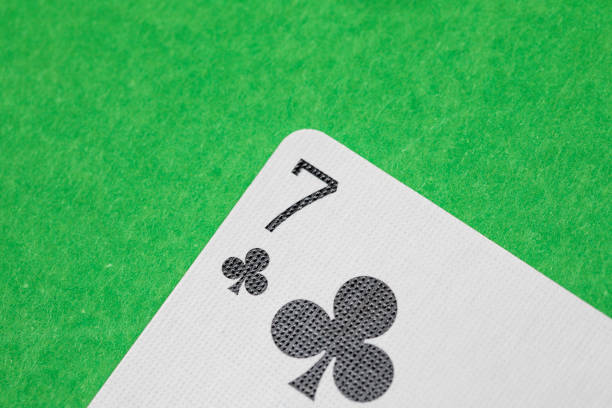 Close up shot of a playing card on a green surface, seven of clubs