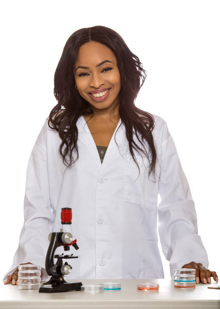 Black female scientist wearing a lab coat with microscope and petri dish doing micro biology research.  She is working in the education or medical industry.  Isolated on white background.