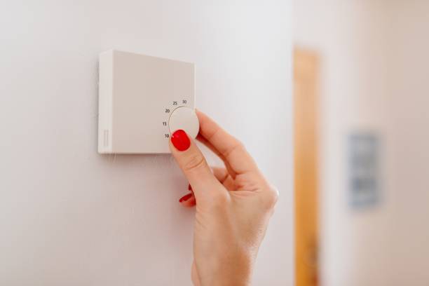 istock Woman regulating temperature on home heating thermostat 887665156