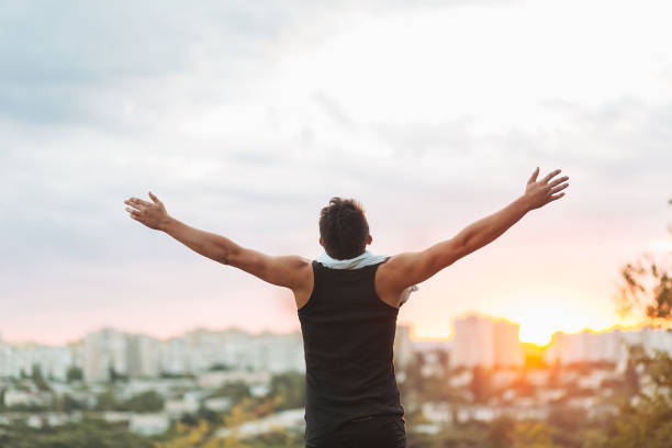 istock Young man raising hands over sunset sky after training 887681424