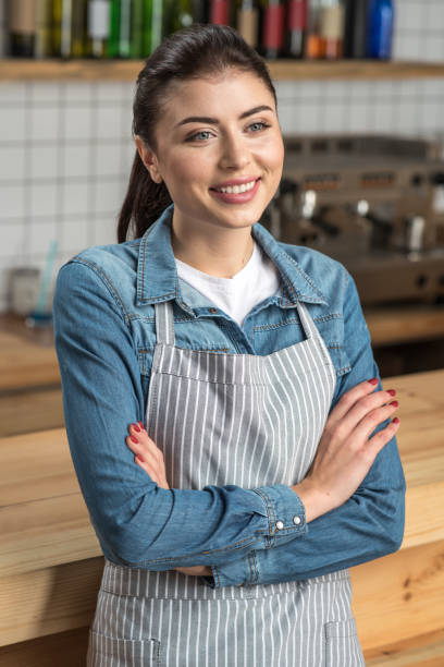 istock Cute young waitress standing with her arms crossed and smiling 887681736