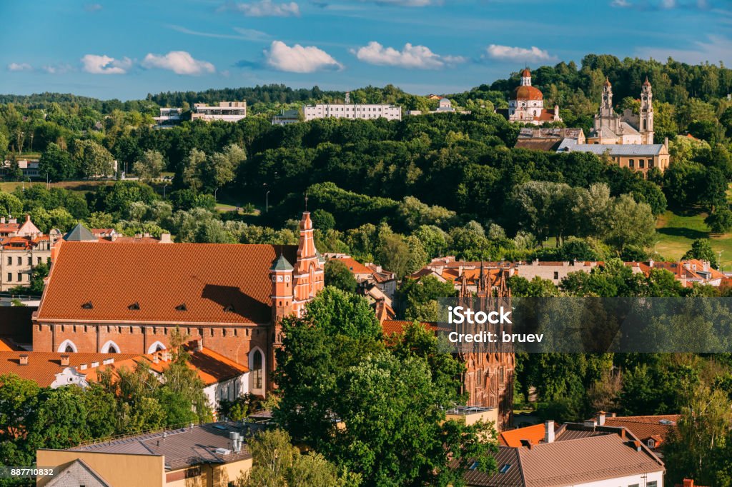 Vilnius, Lithuania. View Of Church Of St. Anne, Church of St. Francis and St. Bernard, Church Of Ascension And Church Of Sacred Heart Of Jesus Vilnius, Lithuania. View Of Church Of St. Anne, Church of St. Francis and St. Bernard, Church Of Ascension And Church Of Sacred Heart Of Jesus Among Green Foliage In Old Town In Summer Day. Ancient Stock Photo