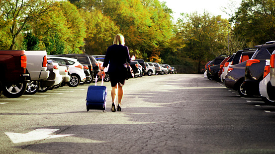 Businesswoman pulling suitcase in parking lot at airport while on mobile phone.