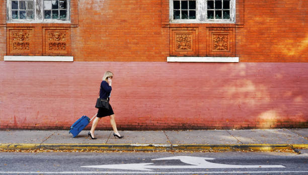 istock Businesswoman pulling suitcase down sidewalk in city. 887711266