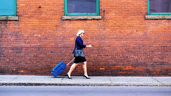 Businesswoman pulling suitcase walking down sidewalk in the city.