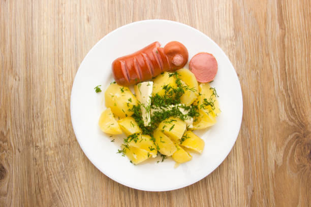 A dish of boiled potatoes and fried sausages on a white plate.