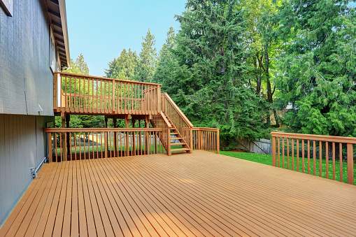 Backyard view of grey rambler house with upper and lower decks and green lawn. Kirkland, WA, USA.