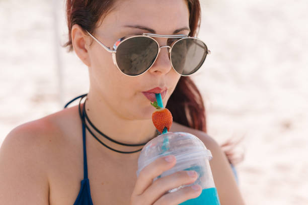 istock Young redhead woman drinking strawberry cocktail on the beach 887798444