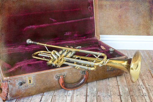 An old rusty trumpet laying on the wood floor sitting in its weathered red velvet lined music case.