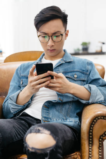 istock Young asian male looking at his mobile device at home 887860390