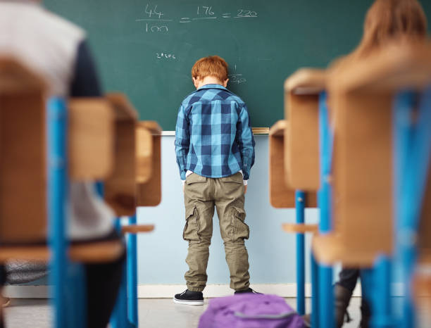 It's no fun feeling like a loser Rear view shot of an elementary school boy leaning with his head on the chalkboard in class sad child standing stock pictures, royalty-free photos & images