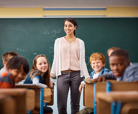 Portrait of a young female teacher standing in a classroom with her students around her