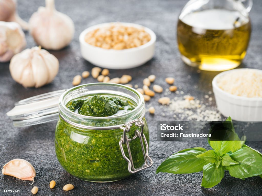 Homemade basil pesto sauce ingredients Homemade pesto sauce and ingredients on dark cement background. Close up wiev of basil pesto in glass jar with ingredients. Appetizer Stock Photo