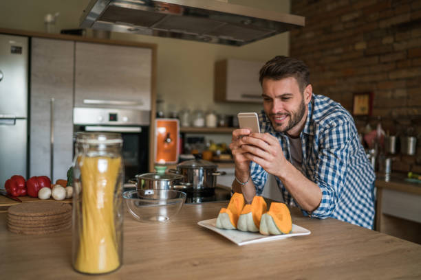 istock Happy man reading recipes on cell phone in the kitchen. 887937604