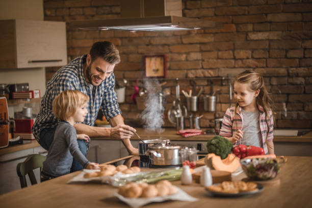 The cutest assistance in the kitchen! happy single father making lunch with his small kids in the kitchen. family dinners and cooking stock pictures, royalty-free photos & images