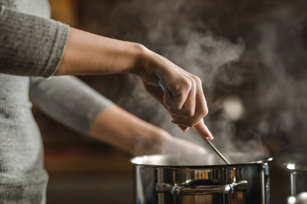 Unrecognizable woman stirring soup in a saucepan while making lunch. Unrecognizable woman making lunch in the kitchen and stirring soup. soup stock pictures, royalty-free photos & images