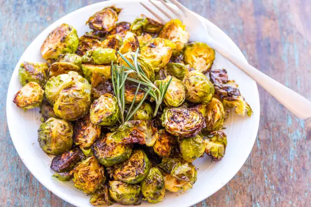 Roasted and Glazed Brussels Sprouts and Rosemary Served in a White Plate with a Fork.