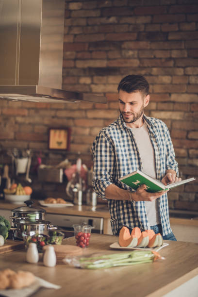 istock Smiling man following recipe from a cookbook in the kitchen. 887954166