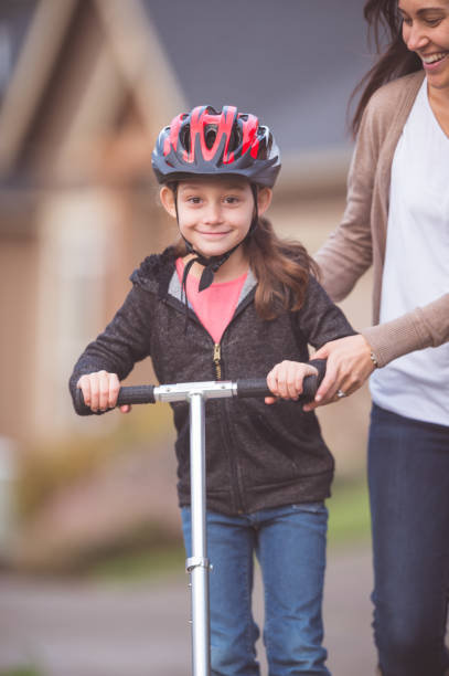 istock Girl Riding Scooter With Mom Coaching Her 887956846