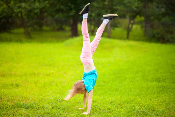 Active little school girl somersault outdoors. Cute athletic schooler girl tumbling, turning, turn handsprings in the park. Sunny summer day. Sport for children. Kid doing gymnastic and having fun. Healty body. handspring stock pictures, royalty-free photos & images