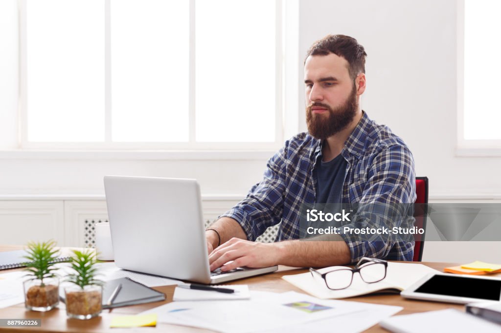 Young concentrated businessman with laptop in modern white office Happy  businessman working with laptop in modern white office interior. Handsome man, successful employee at work with computer. 20-29 Years Stock Photo