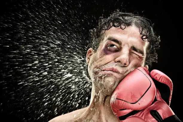 Photo of silly boxer man takes a punch in the face isolated on black.funny concept portrait