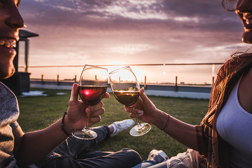 Close up of a couple celebrating their love on a penthouse terrace and toasting with red wine.