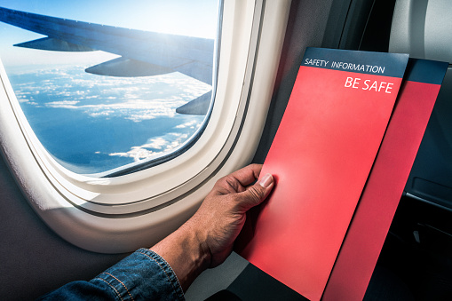 Asian man read flight safety instructions on card board flight. Blank safety instructions on board for passenger and traveler safety.