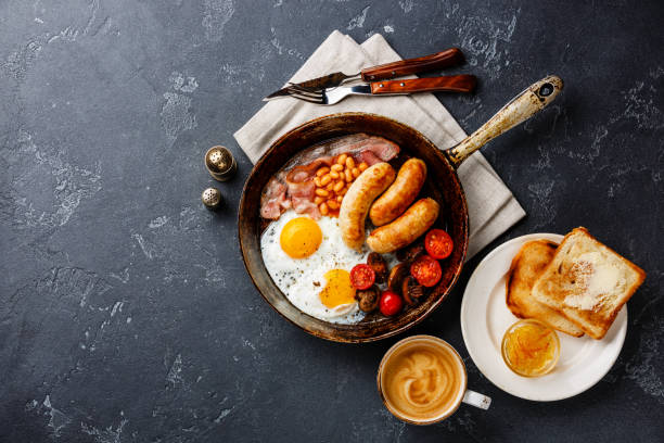 English breakfast in cooking pan English breakfast in cooking pan with fried egg, sausage, bacon, beans, toast and coffee on dark background copy space english breakfast stock pictures, royalty-free photos & images