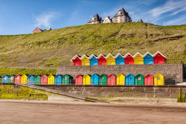 Rows of colorful beach huts on the promenade at Whitby Sands, Whitby, North Yorkshire, England, UK, on a beautiful sunny morning in spring.