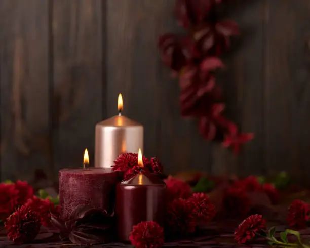 Three candles of crimson and pink color on a dark background with cones, leaves and daisies. Selective focus.