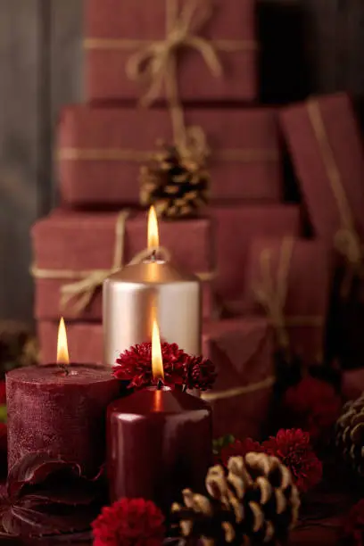 Three candles of crimson and pink color on the background of gift boxes with cones, leaves and daisies. Selective focus.