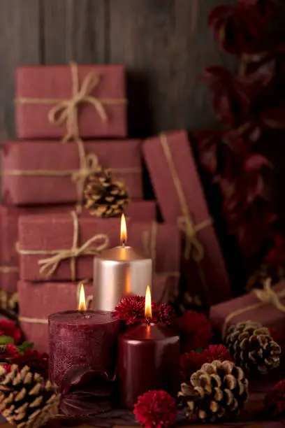 Three candles of crimson and pink color on the background of gift boxes with cones, leaves and daisies. Selective focus.
