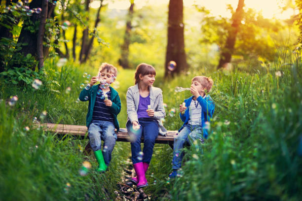 istock Three kids sitting on little bridge and blowing bubbles 888067186